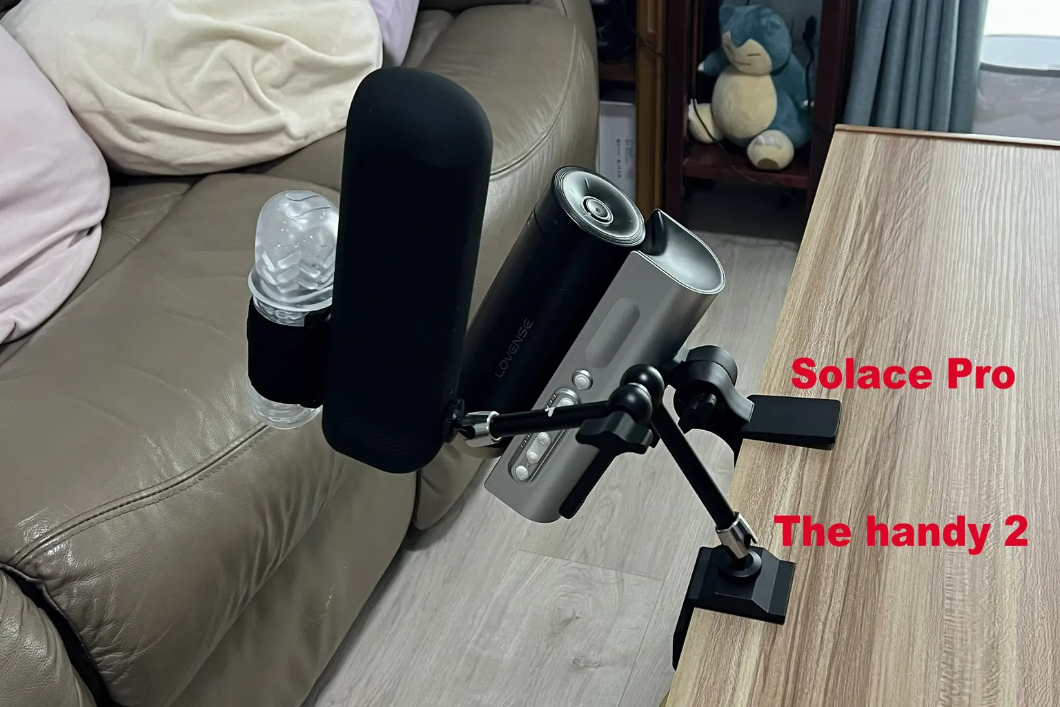Lovense Solace Pro y The Handy 2 instalados uno junto al otro en el borde de una mesa, mostrando las diferencias entre sus soportes, posiciones y ángulos de ajuste